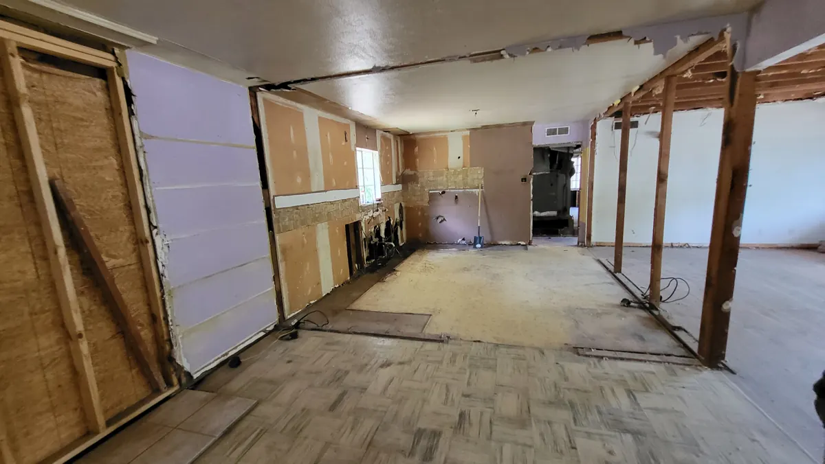 Kitchen during demolition with exposed wall framing and the original window