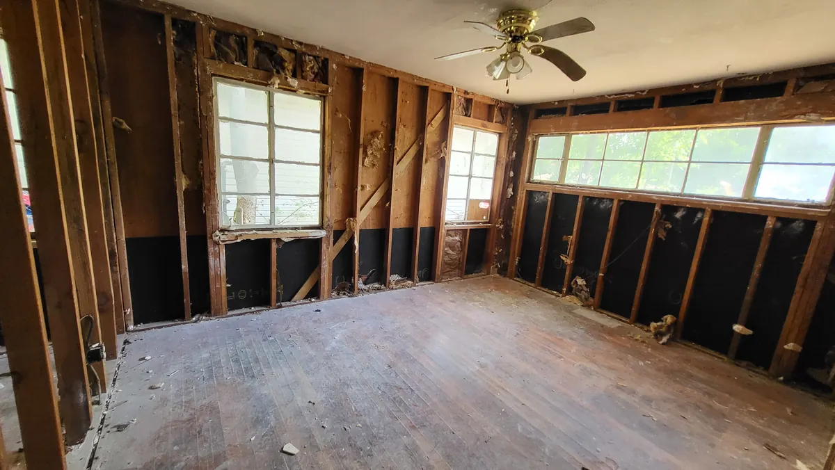 Living room during demolition with a wide corner window and exposed studs